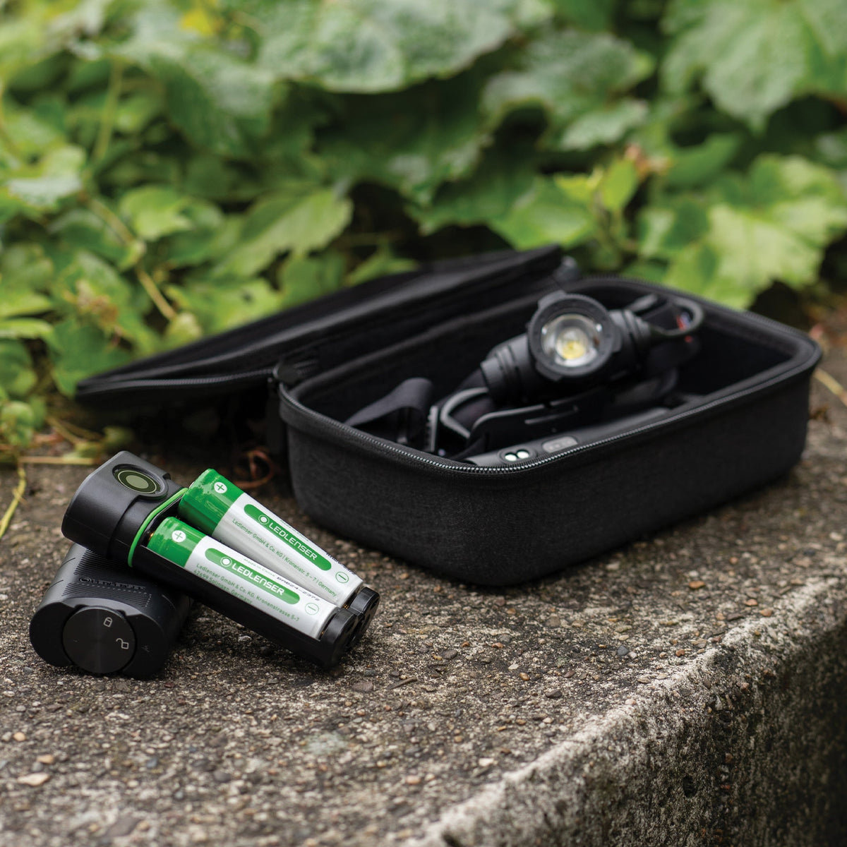 Ledlenser FLEX10 and two 21700 batteries on a stone wall next to a Ledlenser head torch in an open zip case