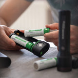 Hands loading two Ledlenser 21700 batteries into the FLEX10 battery sled beside a Ledlenser torch