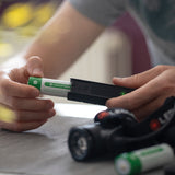 Hands loading a Ledlenser 21700 battery into the FLEX5, with a Ledlenser head torch and spare cell on the table