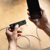 Ledlenser FLEX5 charging a smartphone by cable, held in one hand over a wooden floor