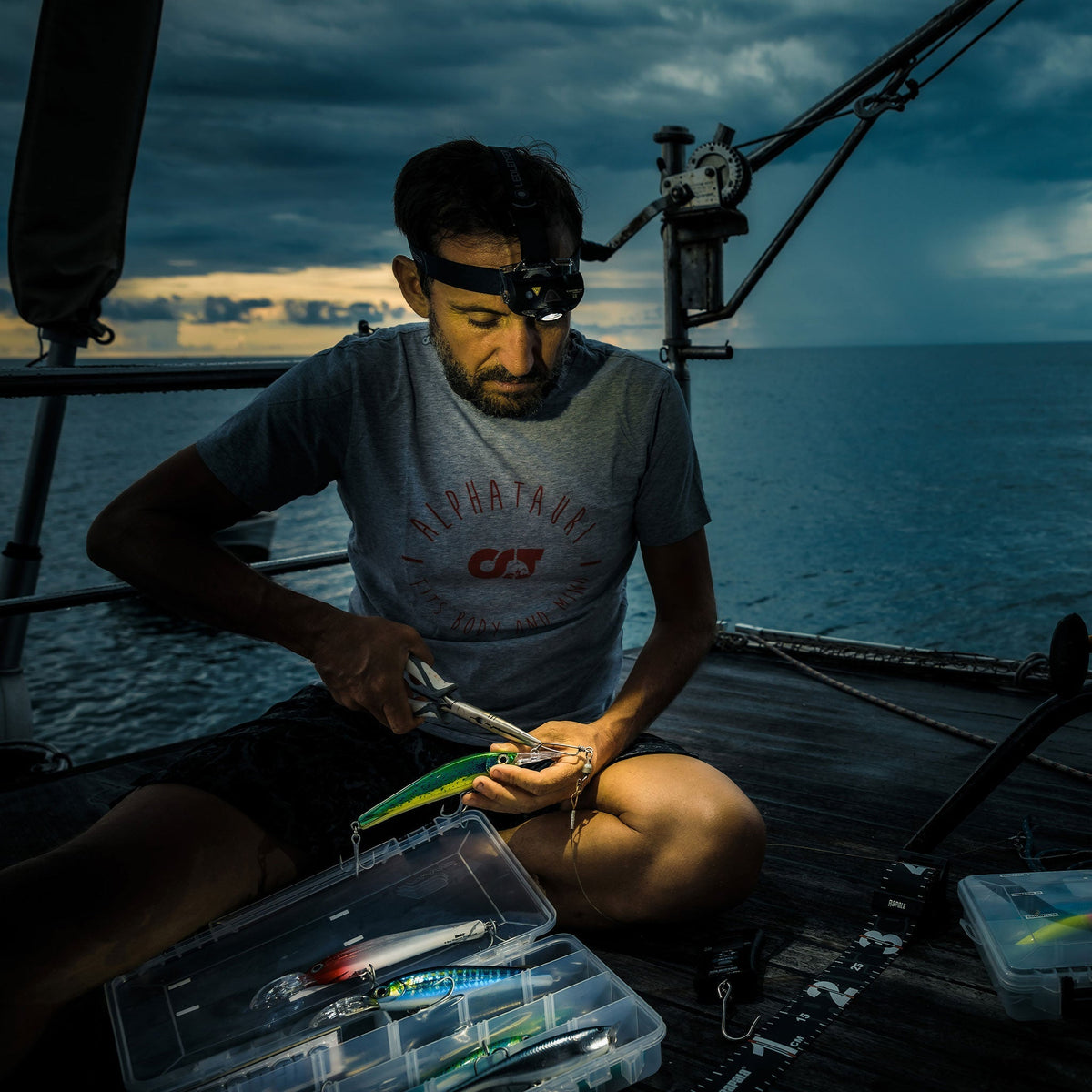 Angler on a boat deck at dusk wearing the Ledlenser MH8 while choosing a lure