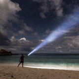 Man on a beach at night pointing the Ledlenser MT14 beam out to sea
