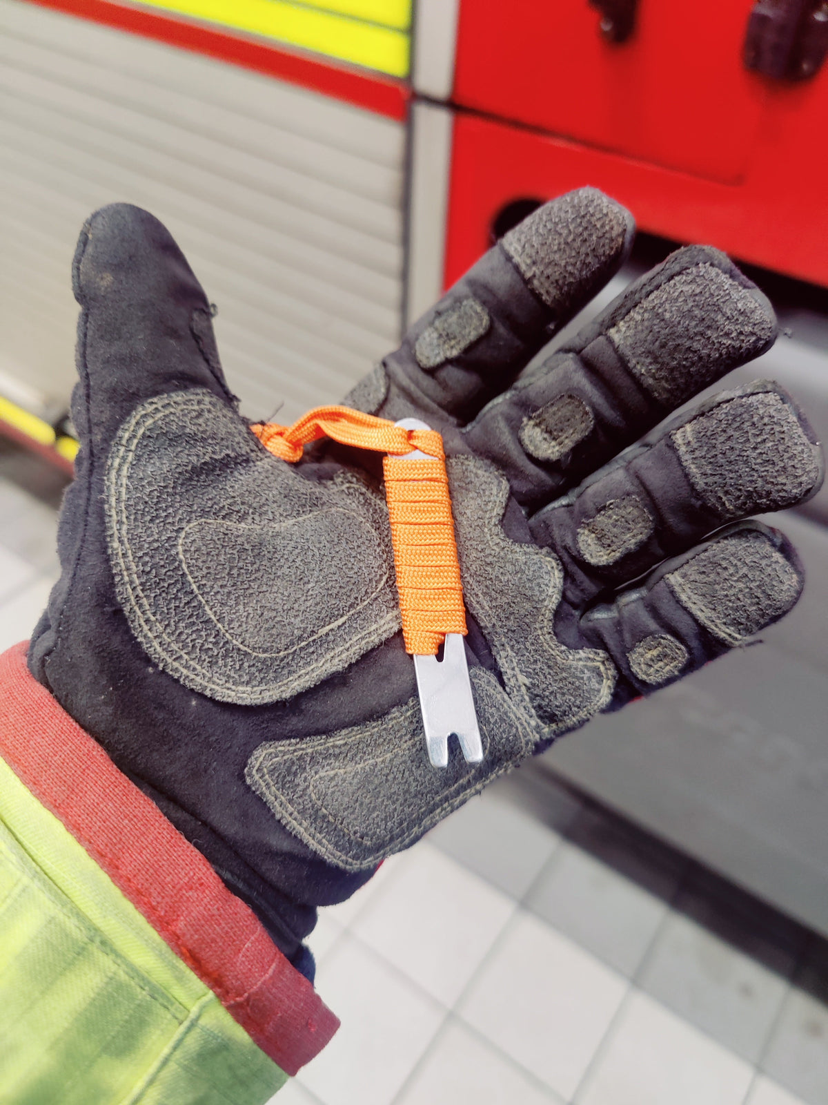 Orange Mini Pry Bar held in a firefighter's gloved hand beside a fire engine locker