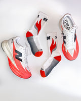 Flat lay of two Stride Ember Ignite running socks between a pair of white and coral running shoes