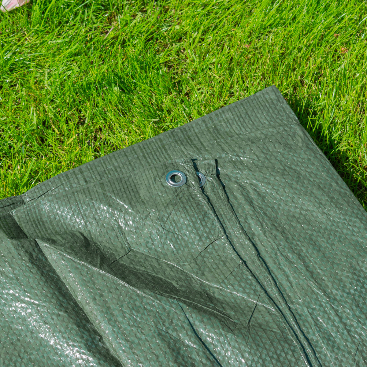 Close-up of the Green S-Grade Tarpaulin 3m x 3m on grass with an eyelet in the hem