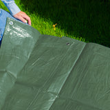 Green M-Grade Tarpaulin 1.5m x 2m spread on a lawn with someone kneeling at the edge