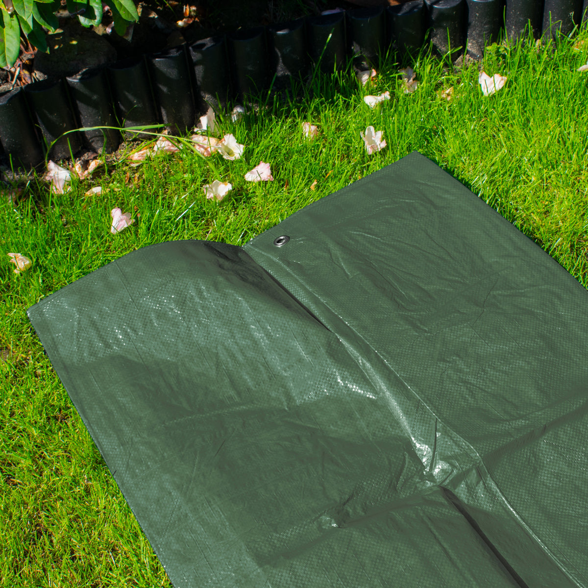 Green M-Grade Tarpaulin with 10m of 6mm Bungee Rope and 10 x Slide Type Tarp Clips laid out on a lawn beside a garden border