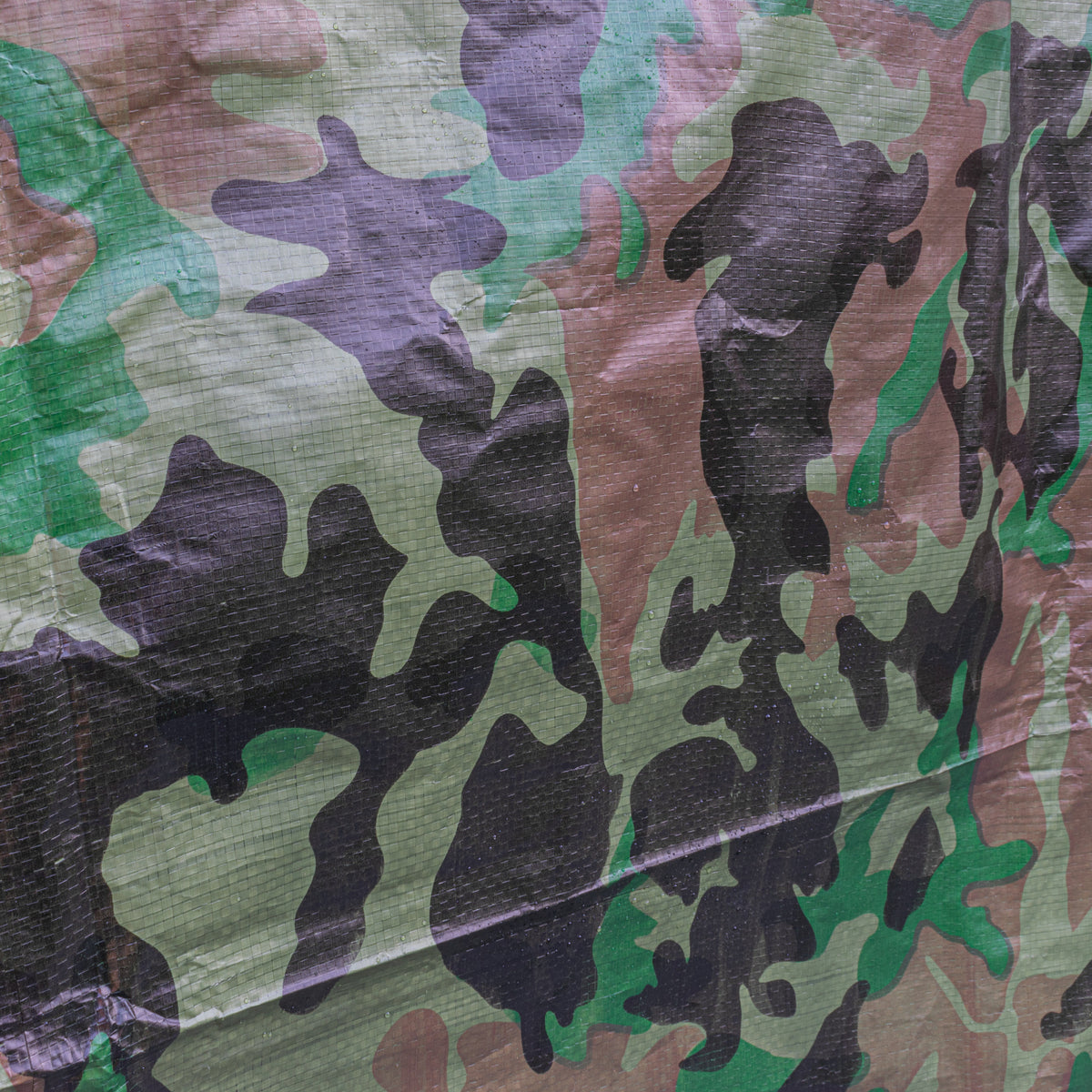 Close-up of the folded edge of the Camouflage M-Grade Tarpaulin 1m x 1m with an eyelet
