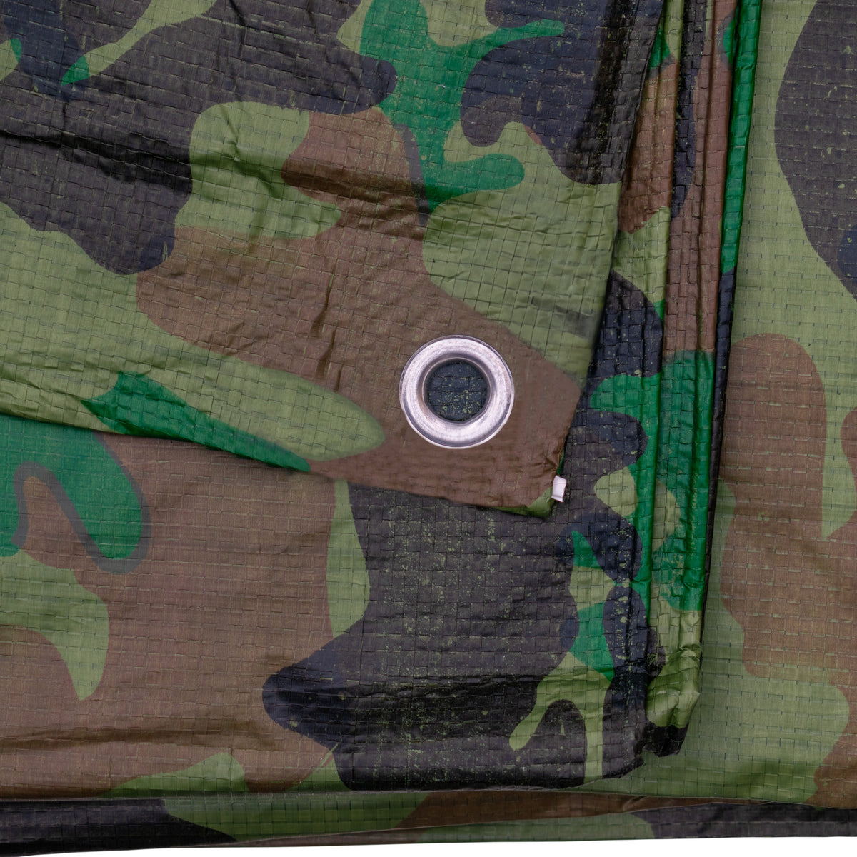 Close-up of an aluminium eyelet in the woodland camouflage fabric of the Camouflage M-Grade Tarpaulin 1.5m x 2.4m