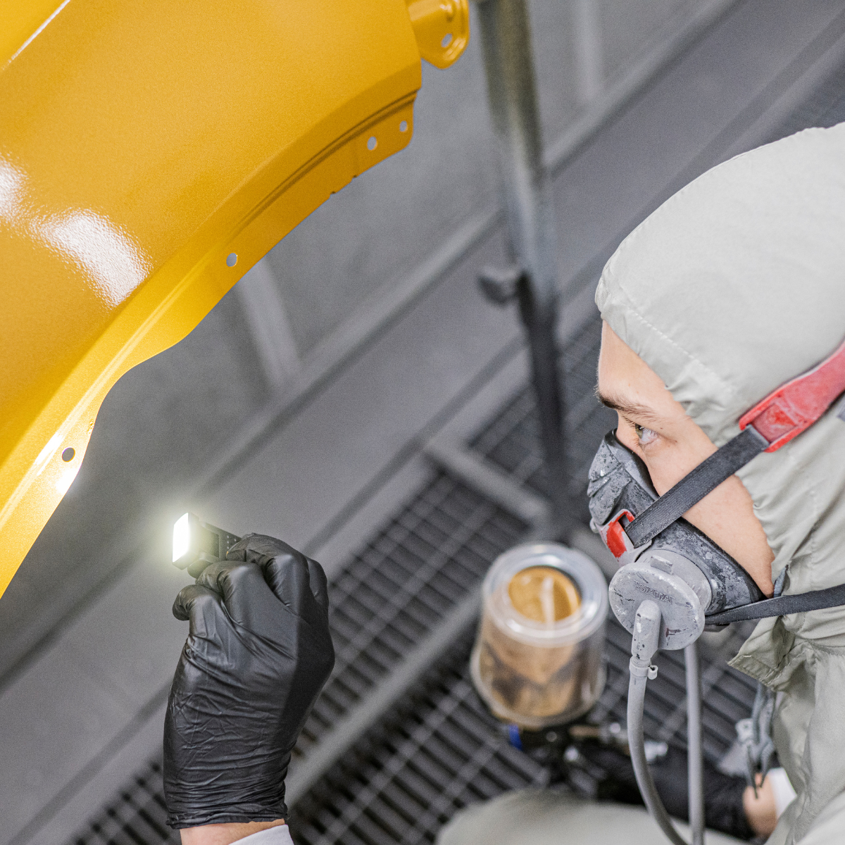 Spray painter in a respirator inspecting a yellow panel with the Ledlenser W1R Work