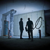 Two workers in a dark unfinished concrete basement, one carrying a Ledlenser AF12R Work lighting the wall ahead