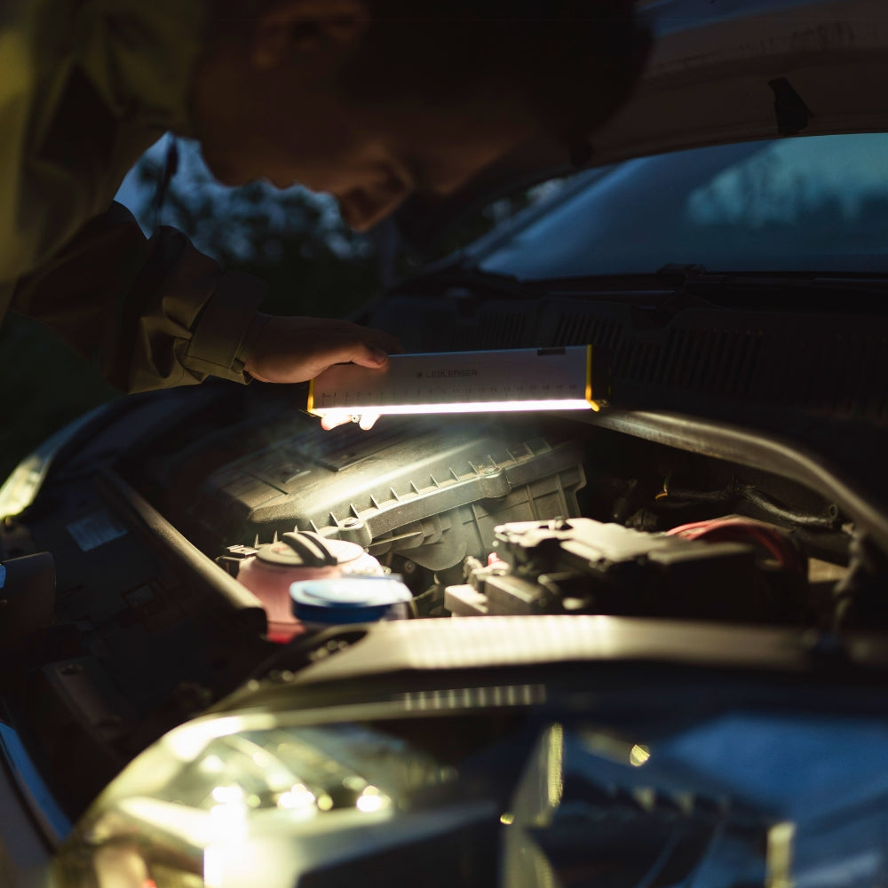 Close-up of a hand holding the Ledlenser AF2R Work low over a car engine at night, light panel facing down