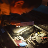 Mechanic holding the Ledlenser AF2R Work over an engine bay, ruler side up, lighting the battery and fluid caps