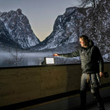 Builder switching on a Ledlenser AF8R Work on a timber balcony at dusk, with snowy mountains behind