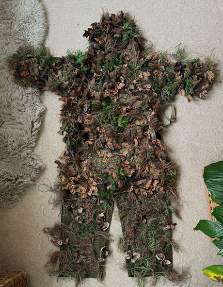 Zero Alpha Designs leaf suit laid out on a floor, a sleeved jacket and separate leg chaps covered in 3D laser-cut leaves and jute strands