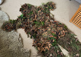 Angled close view of the leaf suit showing layered laser-cut leaves, jute strands and olive elastic loops across the hand-dyed mesh base