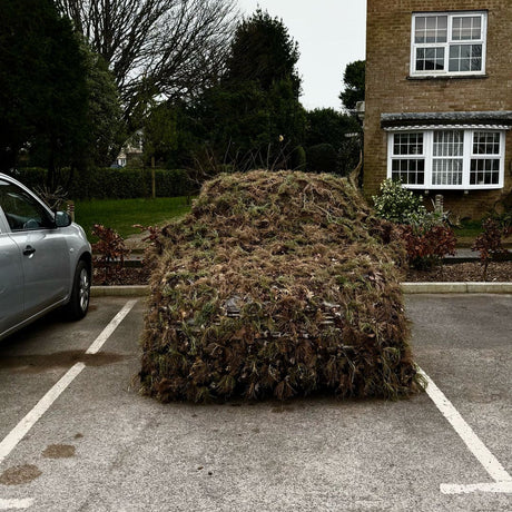 A larger Zero Alpha Designs hide sheet draped over a parked car, hessian garnish covering the bonnet, windscreen and roof