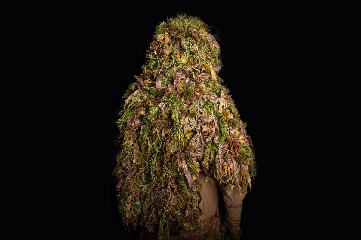 Mid cape ghillie suit shot against a black background, showing the hood and the hessian drape falling to the waist