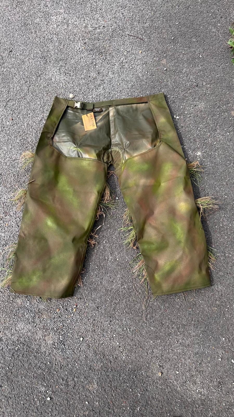 Ghillie chaps showing the waist belt and side-release buckle, the open seat and the waterproof inner face above hand-sprayed green and brown leg panels