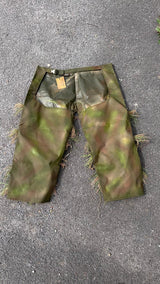 Ghillie chaps showing the waist belt and side-release buckle, the open seat and the waterproof inner face above hand-sprayed green and brown leg panels