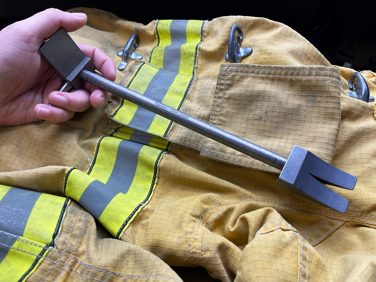 Hand holding the 12 in Titanium Hooligan Bar over a firefighter's tunic