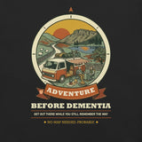 Close-up of the Adventure Before Dementia Campervan T-Shirt print in Vintage Black: a campervan with its awning out by a lake, a couple by a campfire, sheep, hills and a low sun inside a compass badge