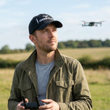 Man wearing the Task "Drone Pilot" cotton twill cap in Black, flying a drone in a grassy English field
