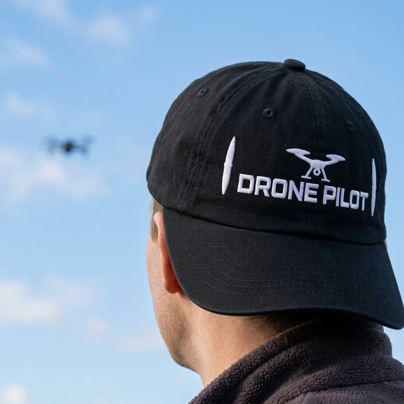 Task "Drone Pilot" cap in Black worn by a pilot watching his drone in a blue sky, showing the white embroidery