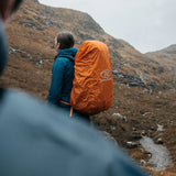 Highlander Duck's Back Waterproof Rucksack Cover in orange from the side outdoors on a hike
