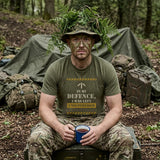 Man in Military Green "Unsupervised" T-shirt with fern-covered hat and face paint, holding a mug of tea on a crate