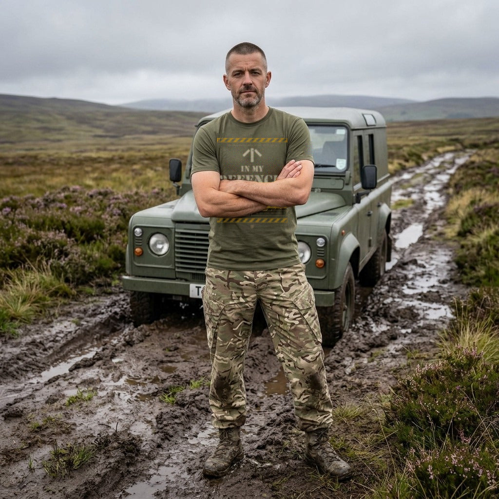 Man in Military Green "Unsupervised" T-shirt, arms folded, beside a 4x4 stuck in moorland mud