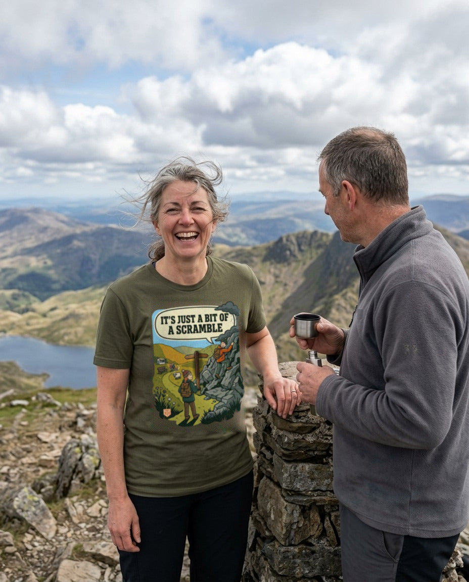 Woman in the It's Just a Bit of a Scramble T-Shirt in Military Green laughing at a summit cairn while her friend holds a flask cup