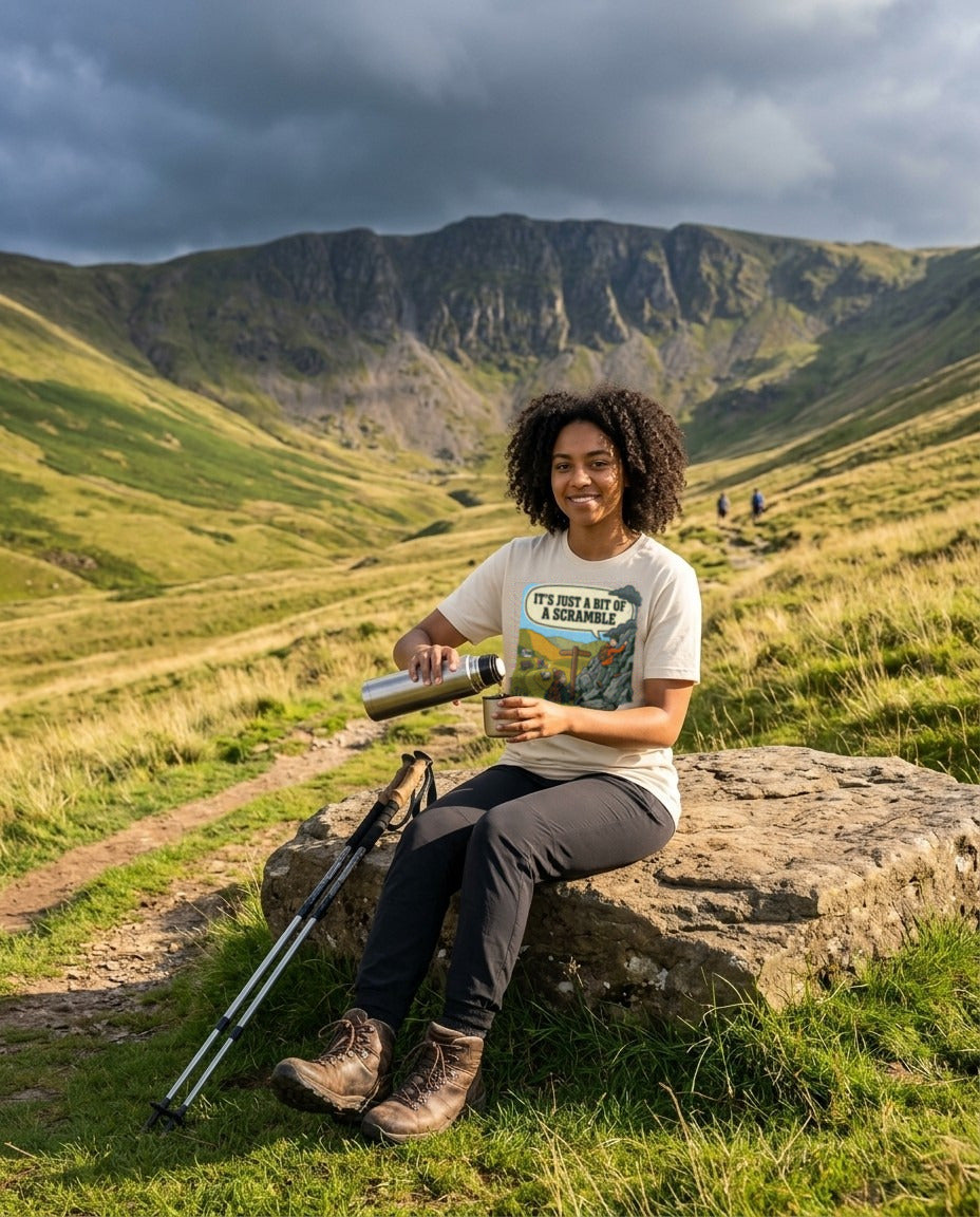 Woman in the It's Just a Bit of a Scramble T-Shirt in Soft Cream pouring tea from a flask on a boulder beside an easy valley path