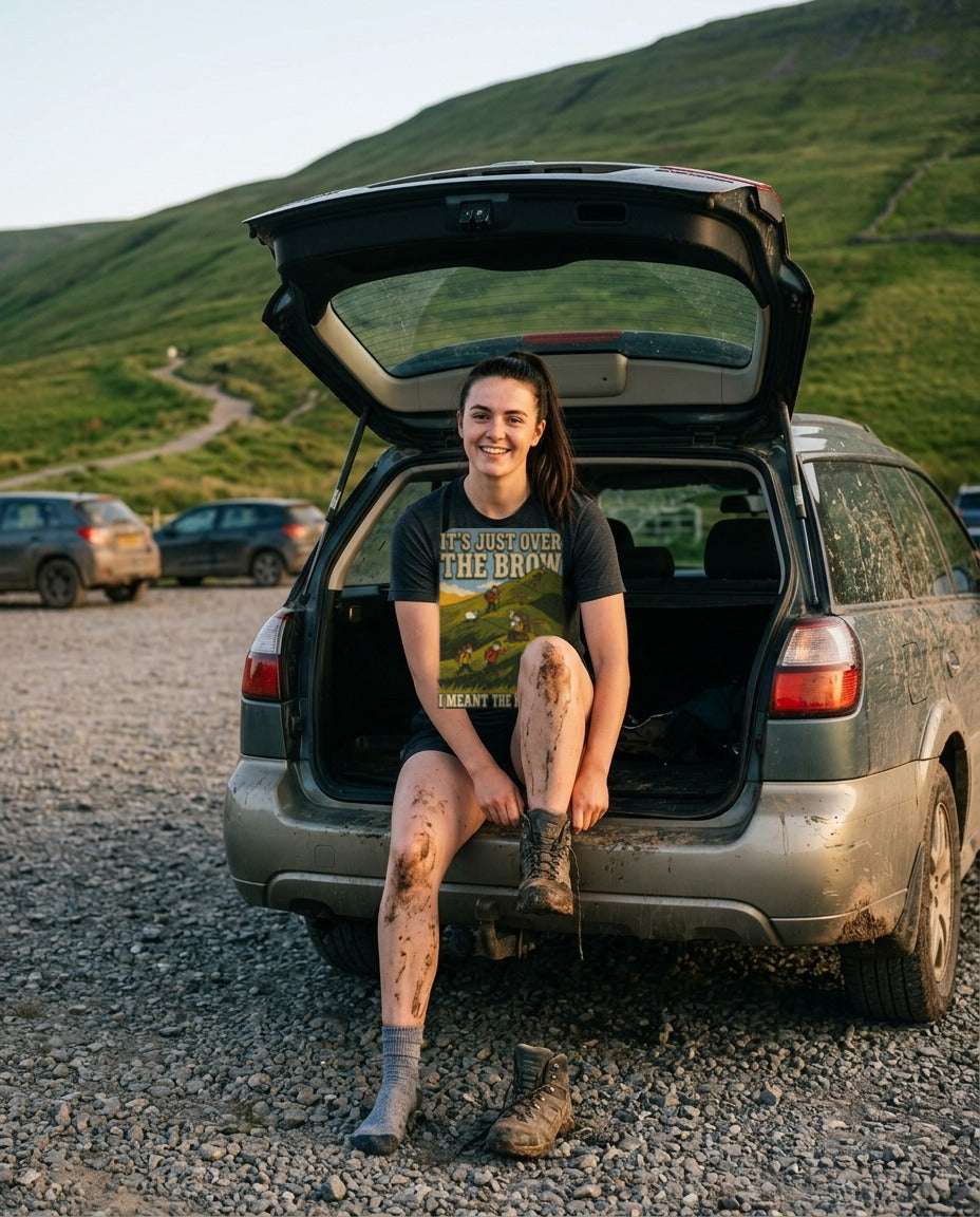 Woman in the It's Just Over the Brow T-Shirt in Dark Grey Heather sitting in the open boot of a muddy car after a hill walk