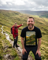 Laughing walker in the It's Just Over the Brow T-Shirt in Vintage Black catching his breath on a hill path while a friend points further up