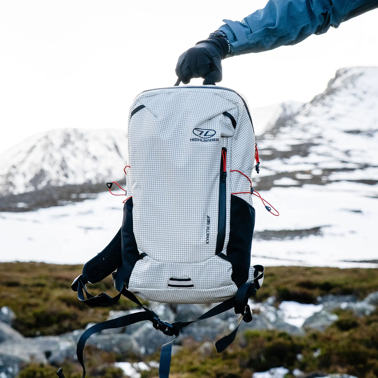 Highlander Kynetik Rucksack 15L in White - held by the grab handle in front of a snowy corrie