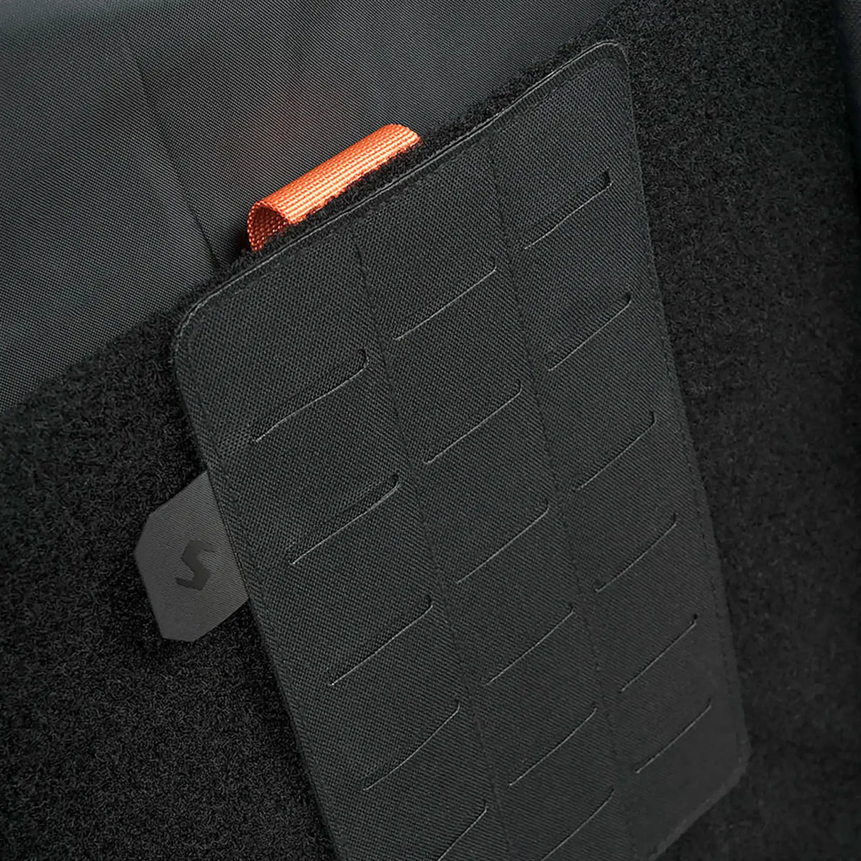 Stoirm Large MOLLE Panel in Black mounted on the hook and loop lining inside a Stoirm pack, showing the laser-cut slots and the Stoirm pull tab