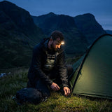 Wild camper with a head torch pushing in the last tent peg at dusk in the Scottish Highlands, wearing the Pitch Late Leave Early T-Shirt in Vintage Black