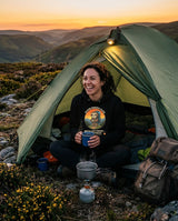 Woman with a brew in her tent doorway at sunset wearing the Sloth Hiking Club: Hilltop Hoodie in Black