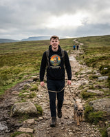 Walker and his terrier on a stony hill path, friends far ahead, wearing the Sloth Hiking Club: Hilltop Hoodie in Black
