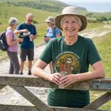 Woman leaning on a field gate on the South Downs while her walking group stops for a brew, wearing the Sloth Hiking Club: Walking T-Shirt in Heather Emerald