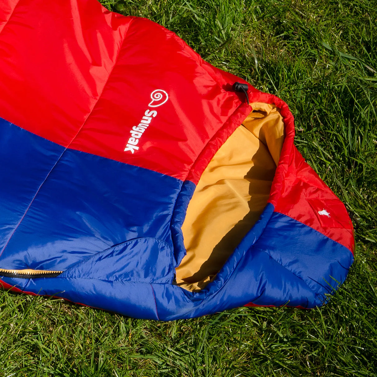 Snugpak Softie Expansion 2 WGTE Sleeping Bag in red and blue - hood and top section on grass, showing the gold inner lining