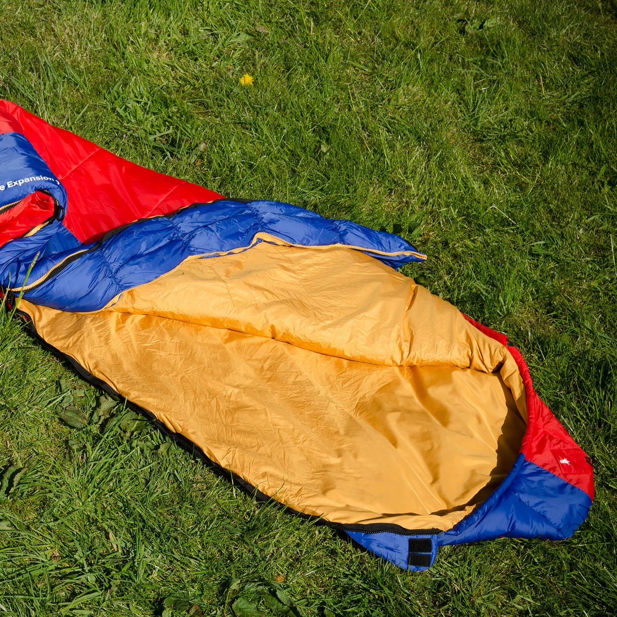 Snugpak Softie Expansion 2 WGTE Sleeping Bag in red and blue, opened flat to show the full gold interior lining on grass