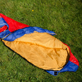 Snugpak Softie Expansion 2 WGTE Sleeping Bag in red and blue, opened flat to show the full gold interior lining on grass