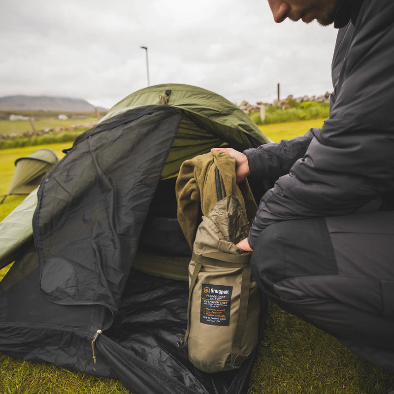 Snugpak Stratosphere WGTE Bivvi Shelter in Olive Green - camper unpacking a sleeping bag beside the pitched shelter