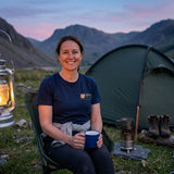 Woman in the Navy Scafell Pike T-shirt with a mug of tea outside a tent at a valley camp at dusk