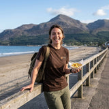 Woman in the Brown Slieve Donard T-shirt eating chips on Newcastle seafront, with the Mourne Mountains behind