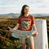 Hiker wearing the Don't Follow Me, I'm Lost Too T-Shirt in Heather Clay, holding a map by a moorland trig point