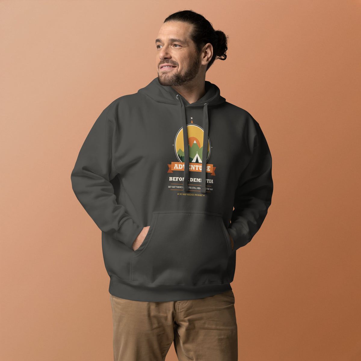 Adventure Before Dementia Camping Hoodie in Vintage Black, worn by a model against an orange background